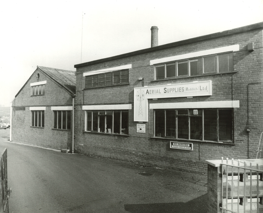 Greyscale photo of a brick building with several large windows and an Aerial Supplies (Redditch) LTD sign.